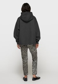 Grauer Kapuzenpullover mit weiten Ärmeln, kombiniert mit eng anliegenden Leggings im Leopardenmuster und schwarzen Slippern. Die glatten Stofftexturen sind sichtbar.