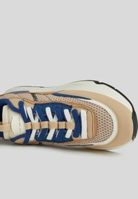 Tenisky se béžovou, modrou a bílou síťovinou, silnou bílou podešví a střídajícími se modrými a bíl�ými šňůrkami na světle šedém pozadí.