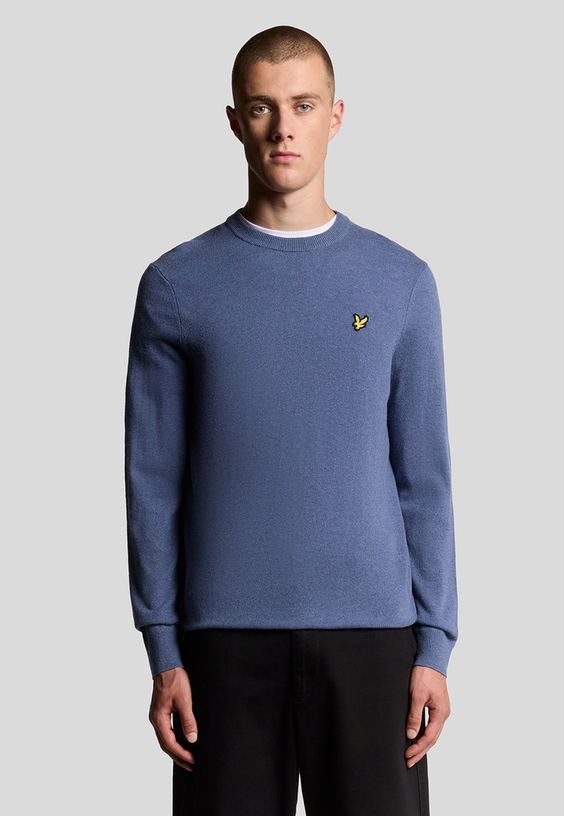 Maglione azzurro a girocollo realizzato in tessuto a maglia, con maniche lunghe e un piccolo logo giallo sul lato sinistro del petto. Texture liscia, vestibilità casual.