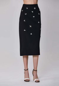 Jupe crayon noire avec des embellissements floraux argentés, taille haute et silhouette droite. Portée avec des escarpins noirs et blancs.