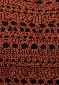 Eisenrostfarbener, offenmaschiger Stoff mit einem Spitzenmuster, das hexagonale und kreisförmige Aussparungen aufweist, kontrastiert mit einem schwarzen Hintergrund.