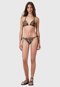 Bikini i leopardmönster tillverkat av ett mjukt material, med en triangulär topp med nackband och lågt skurna bottnar med sidband. Svarta sandaler.