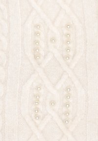 Witte kabelgebreide trui met een gestructureerd patroon en parelaccenten langs verticale lijnen. Het materiaal lijkt zacht en licht glanzend.