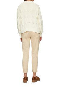 Cremen gestrickter Pullover mit offenem Zopfmuster, geripptem Saum, kombiniert mit beigen, taillierten Hosen und braunen Schuhen, von hinten betrachtet.