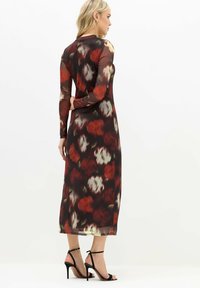 Vestido largo floral con un patrón de rosas en rojo oscuro y blanco, material transparente, mangas largas y un silueta ajustada, combinado con sandalias negras de tacón alto.