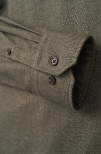 Olive green herringbone fabric with rolled cuff showcasing two brown buttons. Features textured, woven pattern and smooth finish.