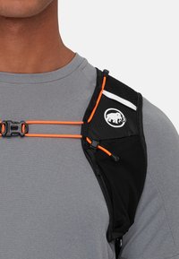 Chaleco de hidratación deportivo negro con acentos naranjas, que presenta una textura de malla, correas ajustables y un parche con logo en el hombro.