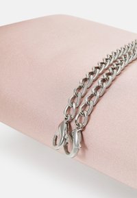 Sølv kædetras med kraftige led og krabbe-lukninger, der hviler på en blød pink overflade. Designet har en blank metallisk finish.