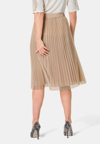 Gelaagde midi-jurk in beige stof met een hoge tailleband. Draagt hoge hakken met een slangenhuidpatroon.