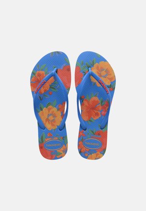 Șlapi albaștri cu modele florale portocalii și galbene și bretele albastre cu numele brandului "Havaianas" scris portocaliu.