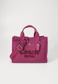 Różowa torebka z płótna z haftowanym logo "Coach New York", podwójnymi uchwytami, regulowanym paskiem i małą metką z logo.