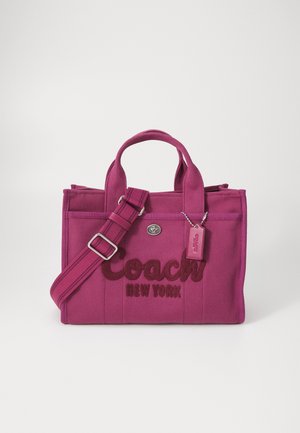 Różowa torebka z płótna z haftowanym logo "Coach New York", podwójnymi uchwytami, regulowanym paskiem i małą metką z logo.