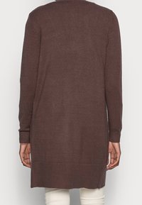 Lang brun strikket cardigan med ribbede manchetter og kant, der har sideslids nederst for øget bevægelsesfrihed. Glat tekstur.