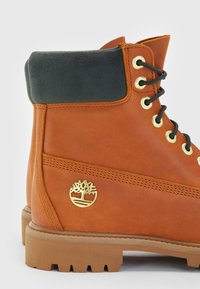 Brązowe skórzane botki za kostkę z ciemnozielonym zamszowym kołnierzem, złotymi oczkami i naszywką z logo. Podeszwa z gumy o ryflowanym bie�żniku zapewniająca przyczepność.