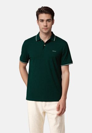 Dunkelgrünes Poloshirt aus Baumwolle mit einer zwei-knopfigen Knopfleiste, kontrastierendem weißen Kragen und Ärmelakzenten sowie einem Logo auf der Brust.