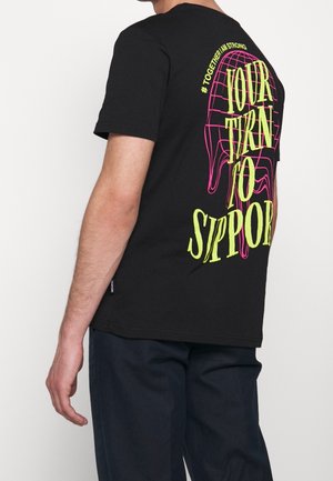 Černé bavlněné tričko s velkým žlutým a růžovým grafickým designem a textem „TVŮJ ČAS PODPOŘIT“ na zádech.