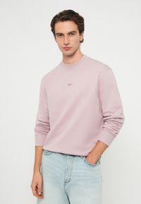 Svetloružová mikina s okrúhlym výstrihom, dlhými rukávmi a rebrovanými manžetami. Na hrudi sa nachádza malé logo „BOSS“ v rovnakej farbe.