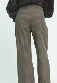 Un pantalon marron à jambes larges avec un motif à fines rayures, doté d'une taille haute et d'une texture douce. Vue de dos montrée.