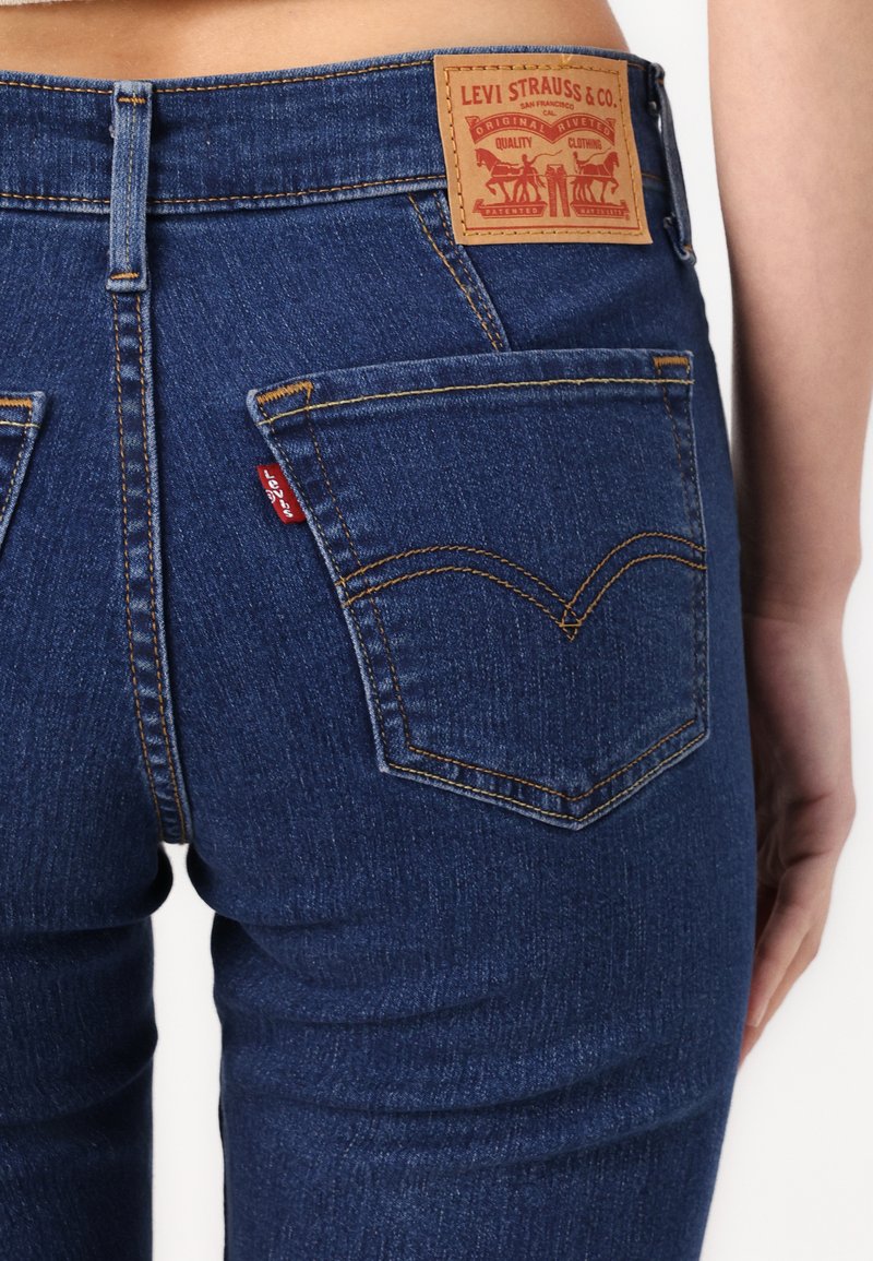 Jeans de mezclilla en azul oscuro con un parche trasero de cuero que presenta el logo de Levi Strauss & Co.; dos bolsillos traseros con costuras en contraste y etiqueta.