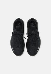 Černé sportovní boty s texturovaným pleteným svrškem, plochými tkaničkami a gumovými podrážkami. Mají logo na jazyku a reflexní prvek na boku.