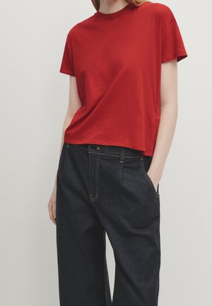 Red cotton t-shirt with a crew neckline, short sleeves, and a relaxed fit, paired with dark blue denim pants featuring side pockets.