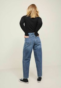 Hellblaue, hochgeschnittene Jeans im lässigen Schnitt mit Gesäßtaschen und gestickten Details, kombiniert mit einem schwarzen Langarmoberteil.