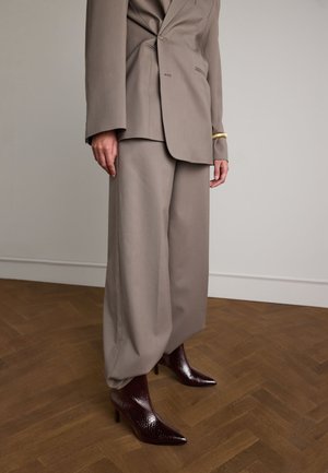 Costume ajusté beige clair avec un pantalon à jambes larges et un blazer structuré. Bottines pointues bourgogne brillante avec une finition texturée.