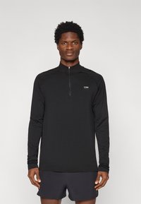 Μαύρο αθλητικό τοπ με μακριά μανίκια, γιακά με μισό φερμουάρ και ανακλαστικό λογότυπο, με λεία υφή και εφαρμοστή σχεδίαση.