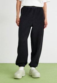 Zwarte fleece joggers met een elastische tailleband, zijzakken en omgeslagen enkels. Zachte textuur en een losse pasvorm voor comfort.