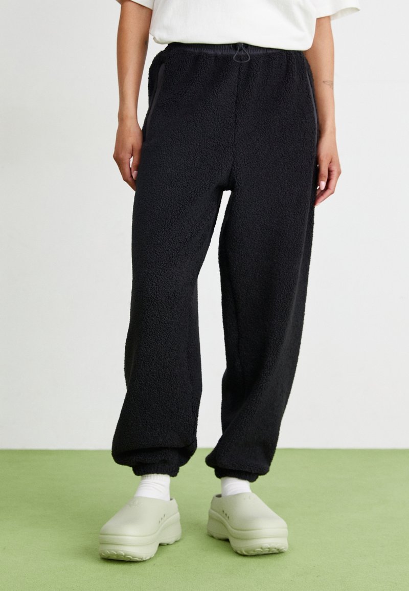 Zwarte fleece joggers met een elastische tailleband, zijzakken en omgeslagen enkels. Zachte textuur en een losse pasvorm voor comfort.