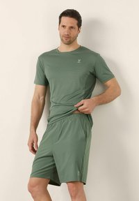 Pánský sportovní outfit s texturovaným, krátkým rukávem, olivově zeleným tričkem a odpovídajícími šortkami s elastickým pasem, obojí vyrobené z lehkého materiálu.