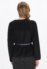 Zwarte, fluffy trui met een brede halslijn en lange mouwen, cinched in de taille met een donkerblauwe riem. Getextureerde gebreide stof.