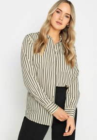 Blusa a rayas en beige y negro, con cierre de botones en la parte delantera, mangas largas y un corte relajado. Tejido suave con un ligero brillo.