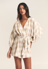 Kremo ir smėlio spalvos languotas kombinezonas su gilia V formos iškirpte, pūstomis rankovėmis ir surišamu juosmens diržu. Lengvas audinys su lygiu paviršiumi.