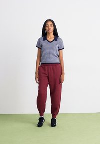 Kortærmet navy- og hvidprikket polo skjorte med v-hals, i kombination med bordeaux sweatpants og sorte træningssko.