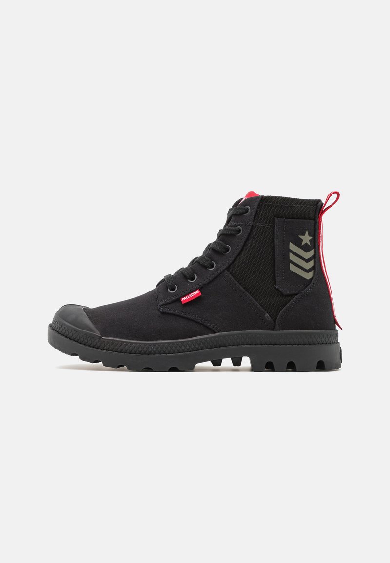 Bottines noires en tissu avec une coque en caoutchouc à l'avant, un panneau latéral texturé, un accent rouge sur le talon, et un patch logo arborant une étoile et des rayures.
