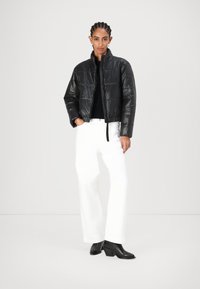 Svart cropped puffer-jakke med høy krage, blank overflate og horisontal søm. Sammen med hvite vid-debber bukser og svarte hæl støvler.
