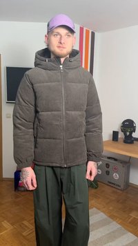 Tumehall metsikübara stiilis sametpüksidega kapuutsiga ja ees tõmblukuga tumehall paks jakk, mis on kombineeritud lahtiste roheliste pükstega. Peal on kanda helelilla nokamüts.