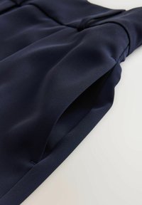 Námořnická modrá tkanina s hladkou texturou, prezentující ruchy a čistý okraj. Design zahrnuje jemný lesk a uhlazené šití detaily.