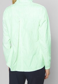 Light green jacket with a subtle wavy pattern, long sleeves, and a back zipper. Soft, lightweight fabric with an elastic hem.