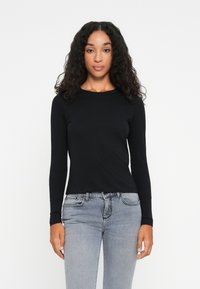 Schwarzes Langarmoberteil aus weichem Material, mit rundem Halsausschnitt und taillierter Passform, kombiniert mit hellgrauen Jeans im klassischen Schnitt.