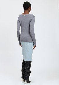 Langärmliges graues Strickoberteil mit weitem Ausschnitt, kombiniert mit einem hellblauen Denim-Bleistiftrock und schwarzen kniehohen Stiefeln mit Absatz.