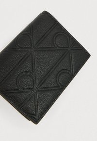 Μαύρο δερμάτινο πορτοφόλι με ανάγλυφο γεωμετρικό σχέδιο, με υφή στην επιφάνεια και καθαρές γραμμές, γωνιακές άκρες και μίνιμαλ σχεδιασμό.