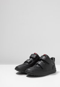 Sneaker nere con doppie cinghie in Velcro, materiale sintetico testurizzato, punta arrotondata e suola in gomma. Presenta dettagli del logo in rosso.