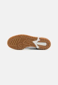 White athletic shoe sole with a textured gum rubber outsole, featuring a pattern of grooves and strategic tread for traction.