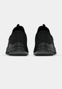 Coppia di scarpe da ginnastica nere viste da dietro, con linguette per facilitare l'indossamento e suole intermedie testurizzate.