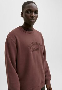 Maroon sweatshirt with a round neckline, featuring “ORIGINALS” embossed on the front. Made from a soft fabric with a relaxed fit.