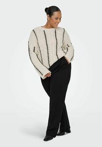 Pull en tricot torsadé crème avec des détails de couture noirs, associé à un pantalon noir. L'ensemble présente une coupe décontractée et un design simple.