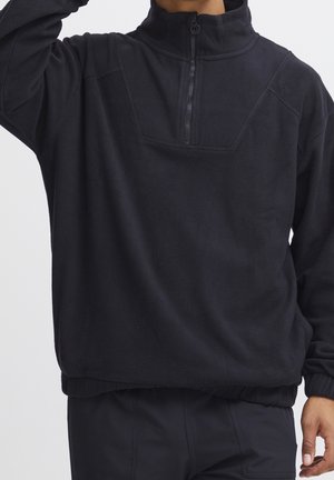 Zwarte fleece trui met een hoge kraag, halve rits aan de voorkant en geribde zoom. Heeft een subtiel gestructureerd patroon op de stof.