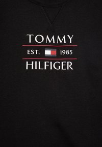 Fekete pulóver, fehér "TOMMY HILFIGER EST. 1985" felirattal és piros-kék logóval. Sima anyag, bordázott nyakkivágással.